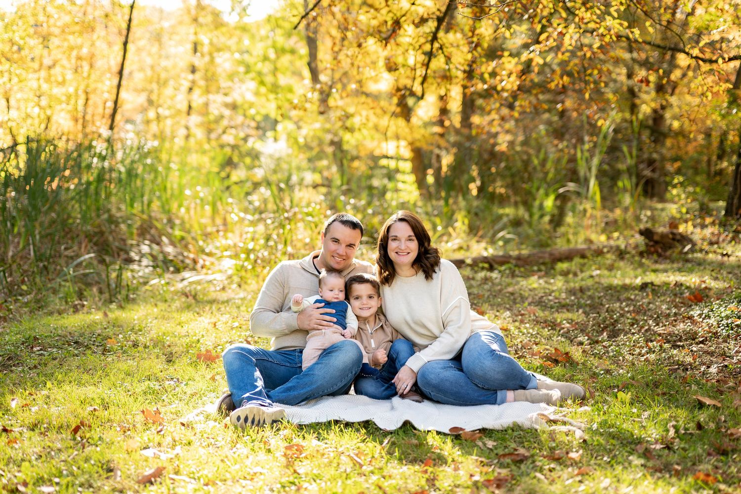Happy family of four sitting on blanket surrounded by golden fall foliage in a sunny park.