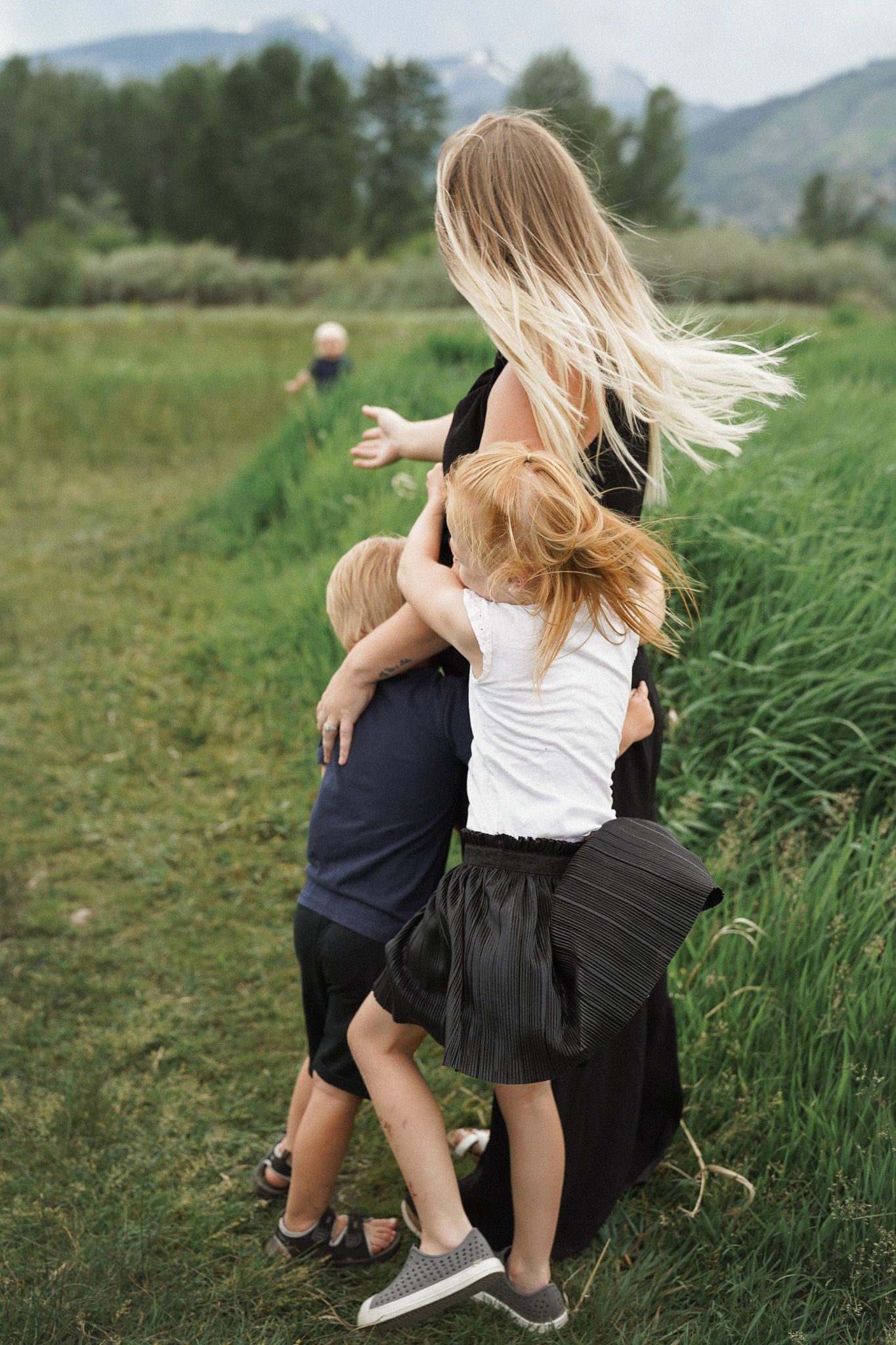 Spontaneous dance moment captured in a meadow with tall green grass and mountains in the background.