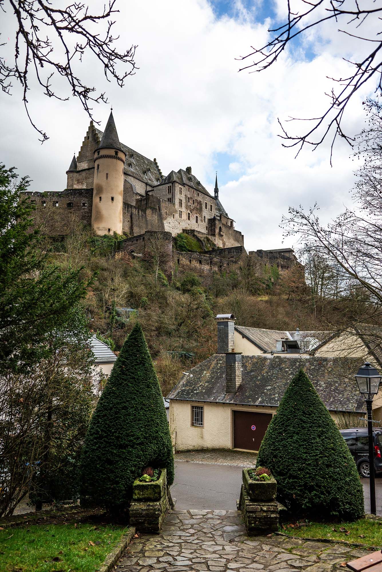 Medieval castle perched on a hilltop with manicured topiary gardens and stone pathways leading to the entrance.