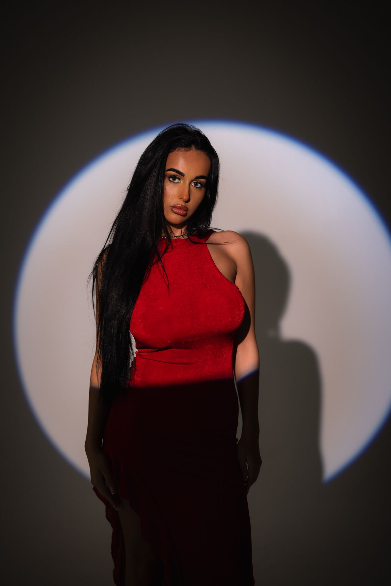Dramatic portrait series in red dress against dark background with spotlight creating moody shadows and contrast.
