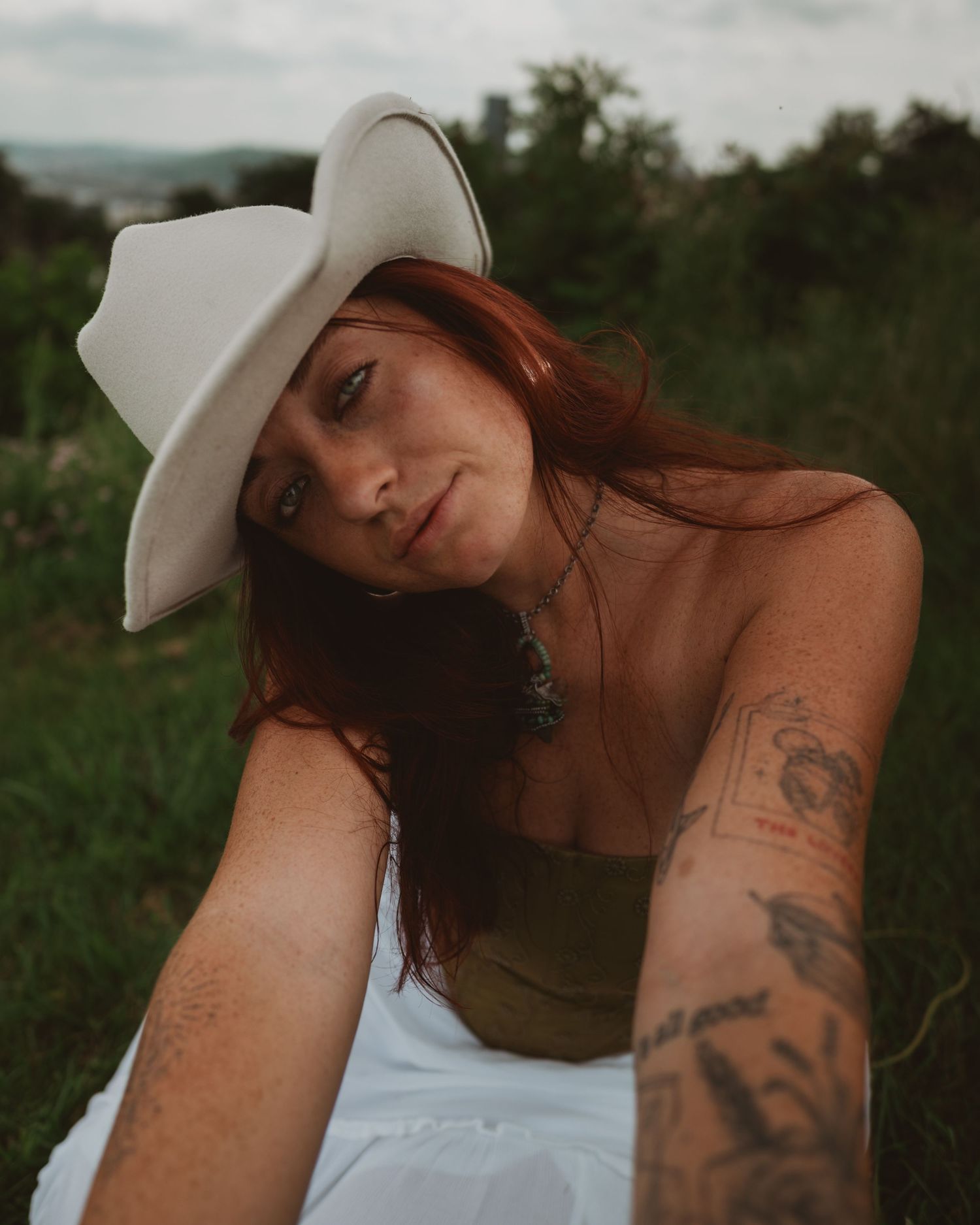 A series of artistic outdoor portraits showing a person in a white hat and olive top with visible tattoos in a natural setting.