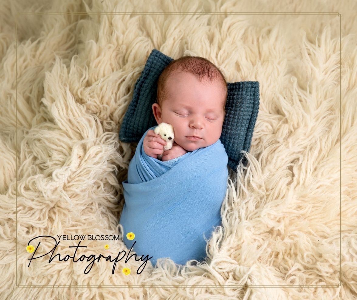 Peaceful sleeping newborn wrapped in soft blue swaddle blanket lying on cream-colored furry backdrop.