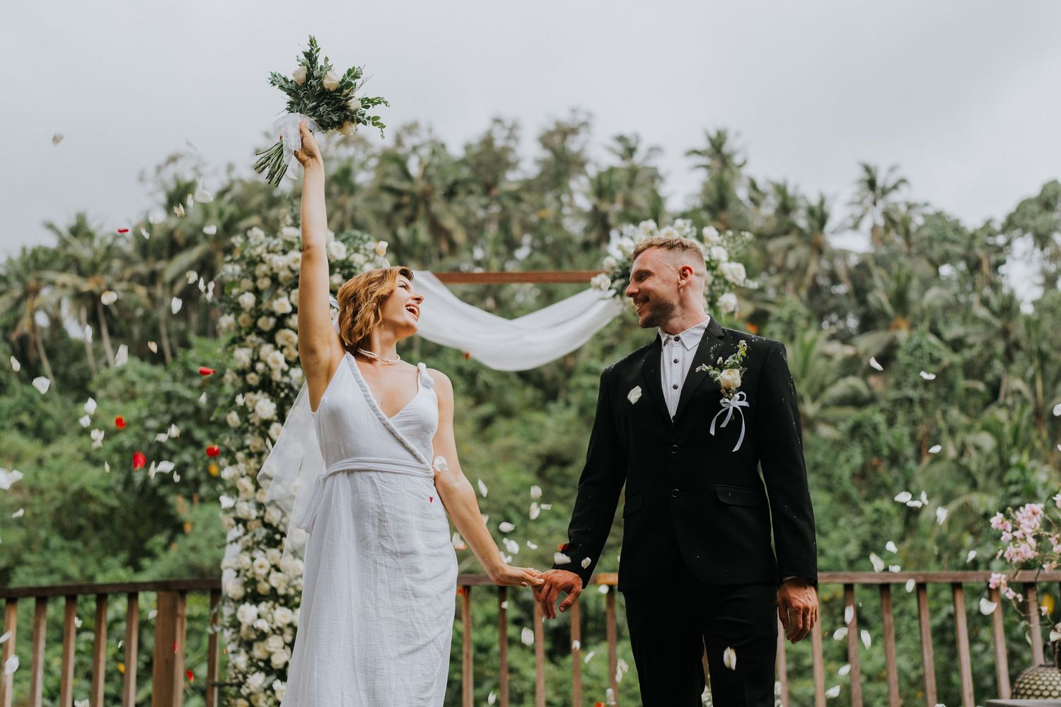 Outdoor wedding ceremony in tropical garden setting with white decor.