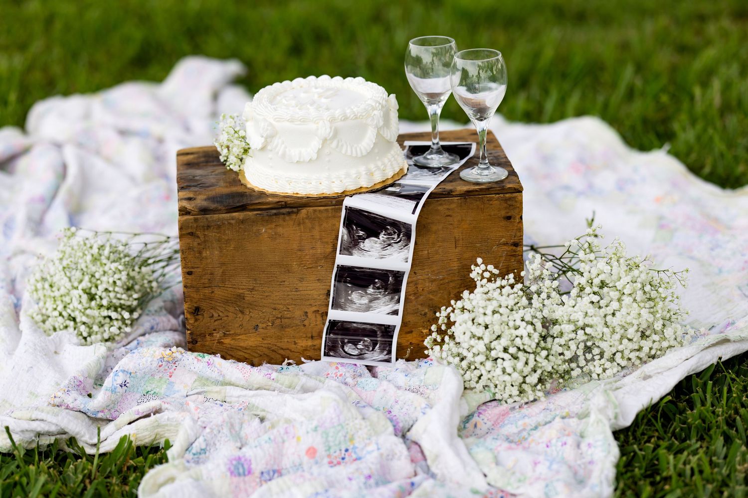 Rustic wood box decor arranged with baby's breath flowers and wine glasses on white linen for outdoor picnic setting.