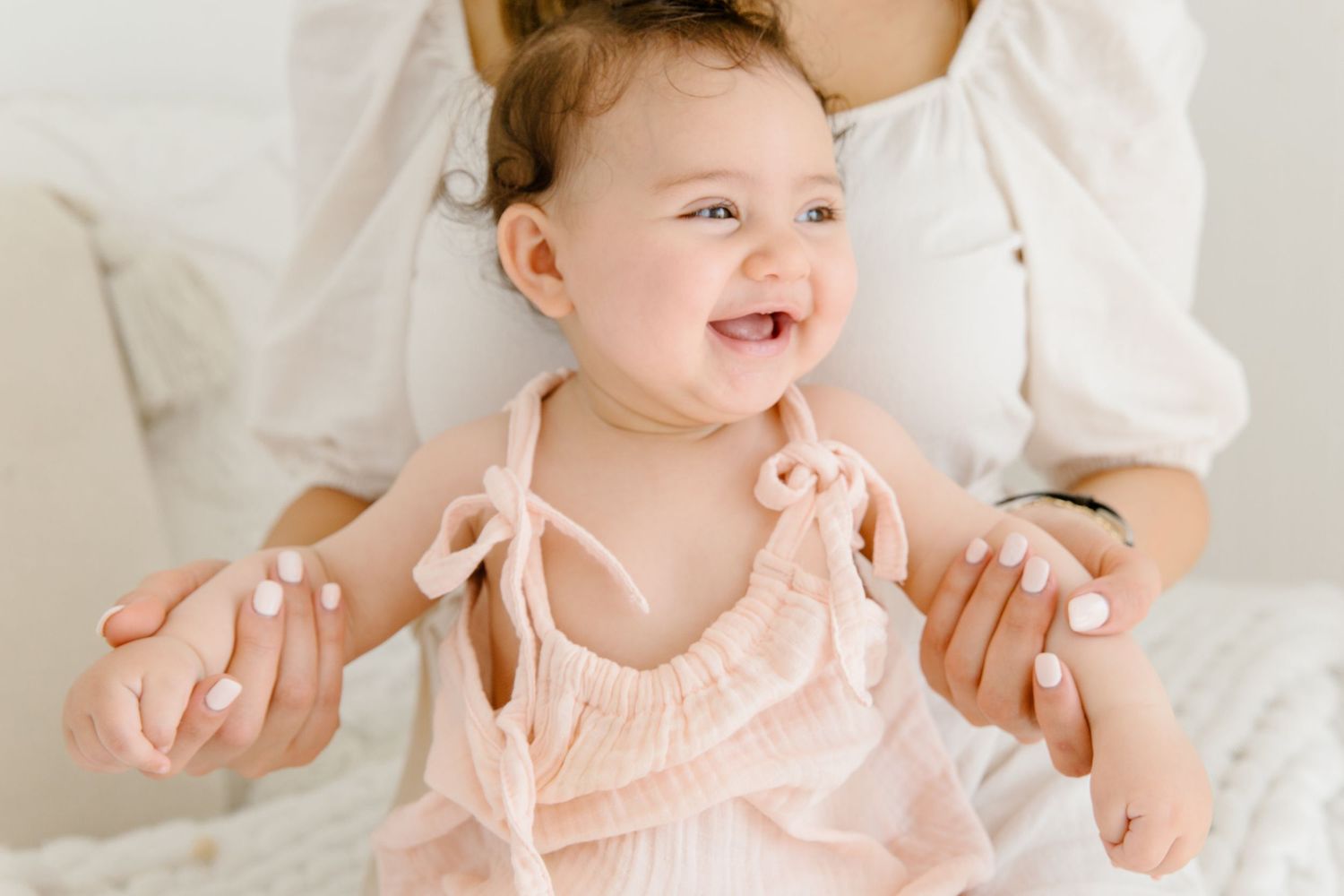 Baby in a pink ruffled dress smiling and playing.