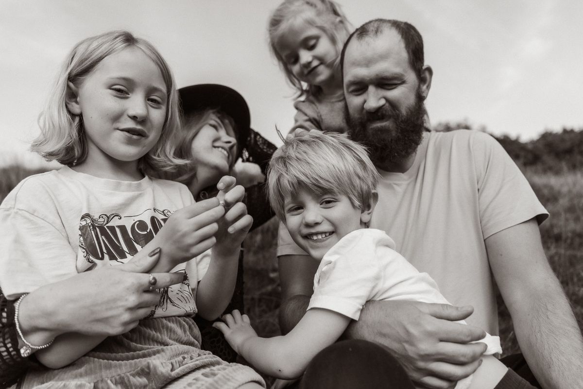 A candid black and white portrait shows a family of five outdoors sharing a playful moment together.