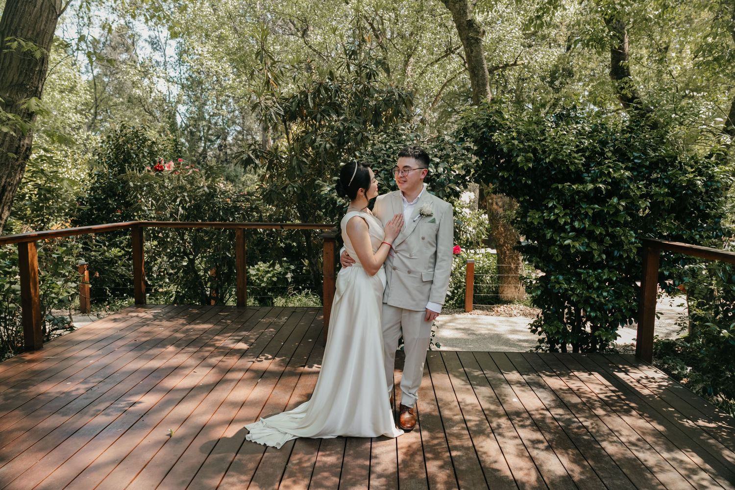 Couple sharing tender moment on rustic wooden deck surrounded by lush greenery during outdoor garden wedding ceremony.