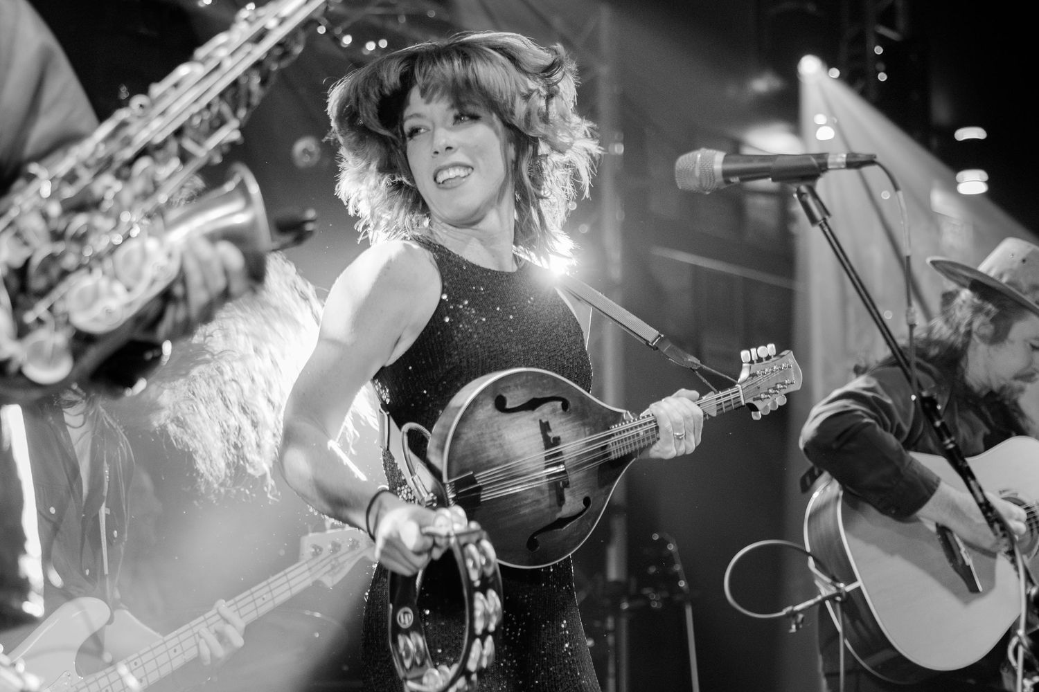 Musicians performing with mandolin and horn instruments in dramatic black and white lighting.