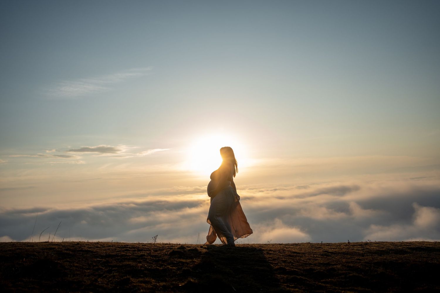 A silhouetted figure walks along a hill against a dramatic sunset with clouds in the background.