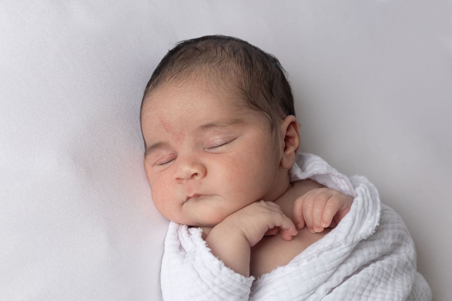 Newborn baby girl peacefully sleeping in neutral-toned wrap during Benfleet studio photography session
