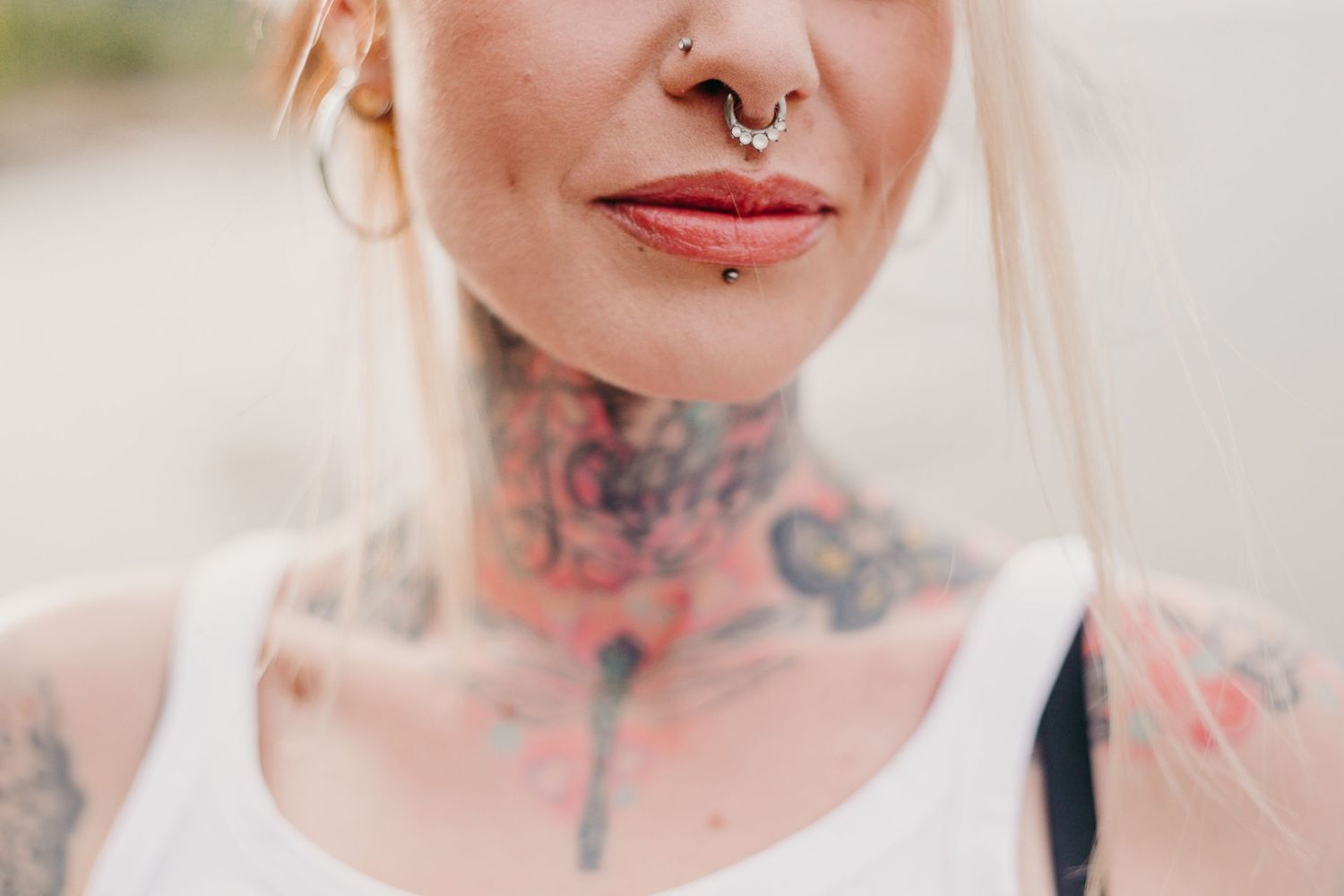 Close-up shot of neck tattoos and a septum piercing against blurred background.