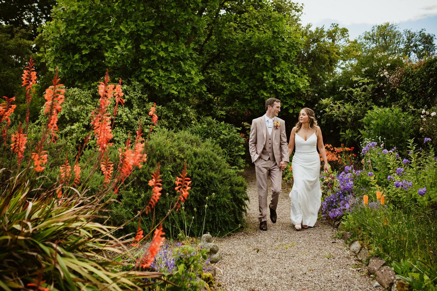 A couple walks along a garden path lined with vibrant red and purple flowers.