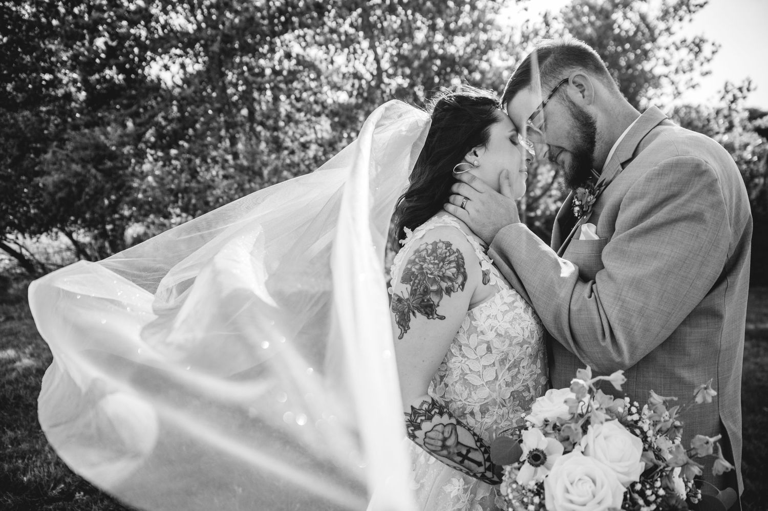 A black and white portrait of newlyweds sharing an intimate moment with flowing veil.