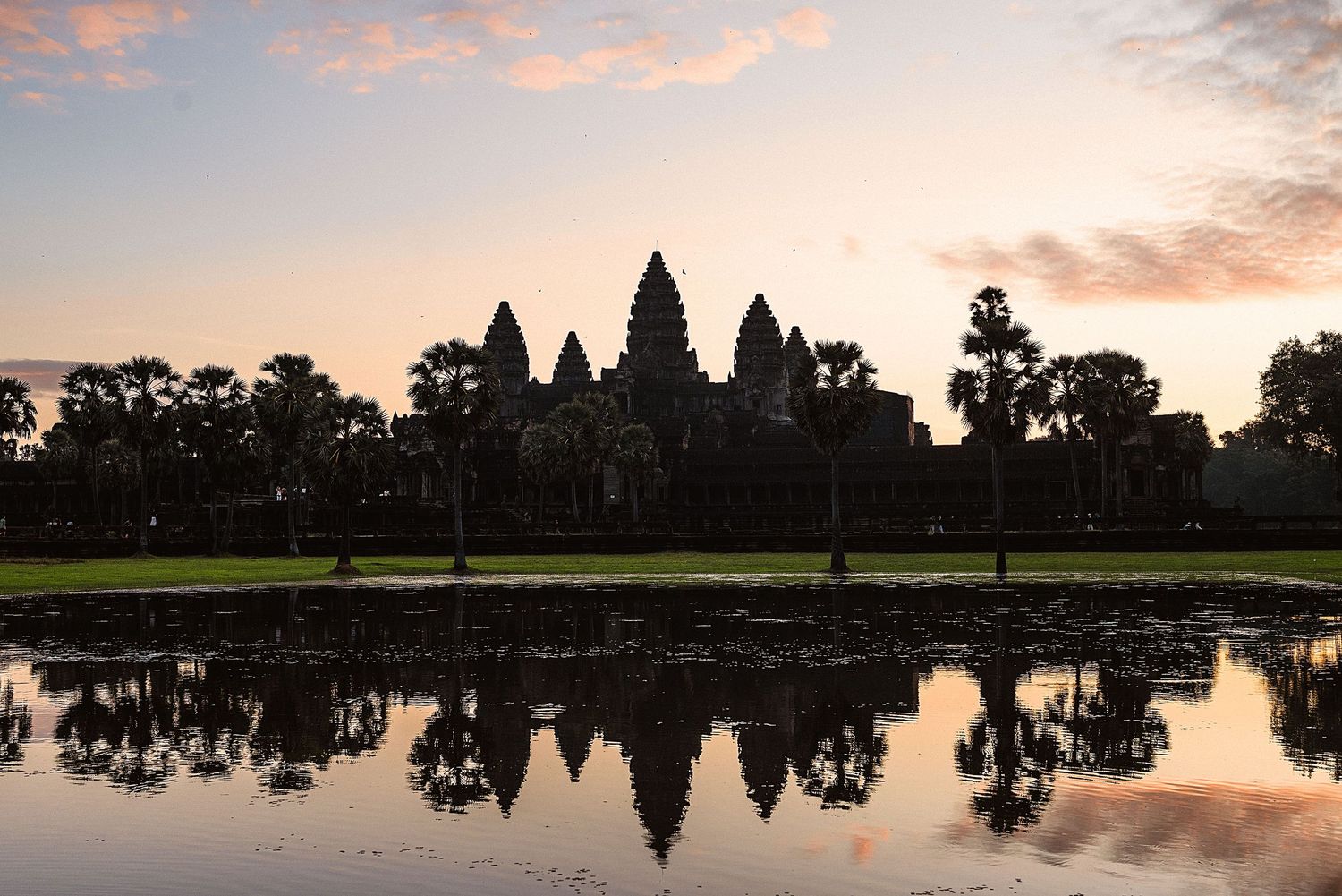 Silhouette of Angkor Wat temple reflected in still water during sunset.