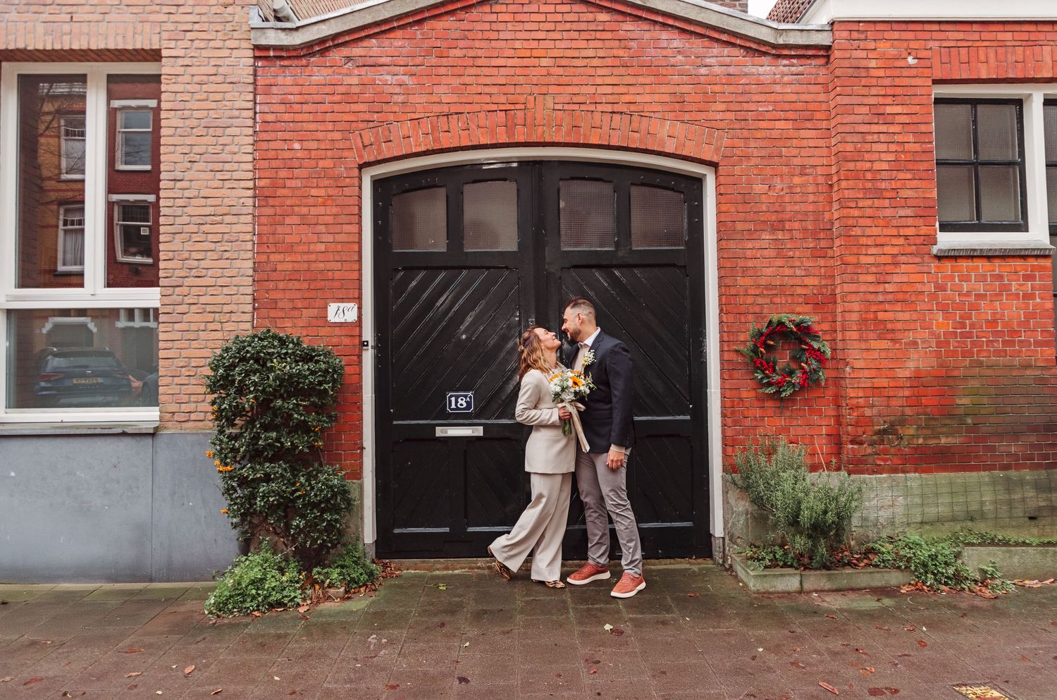 A bridal couple posing together against a building with brick walls.