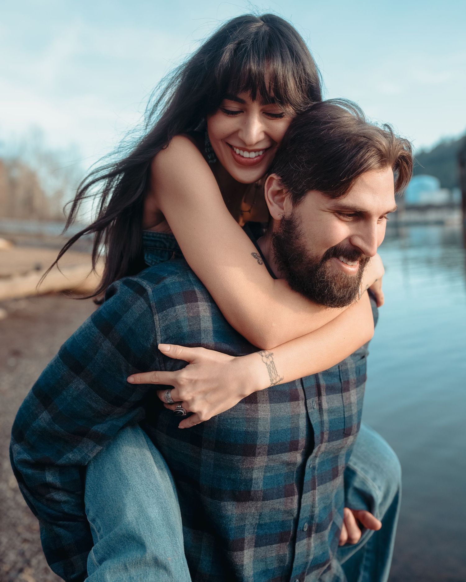 Couple enjoying a playful piggyback ride by the water on a sunny autumn day.