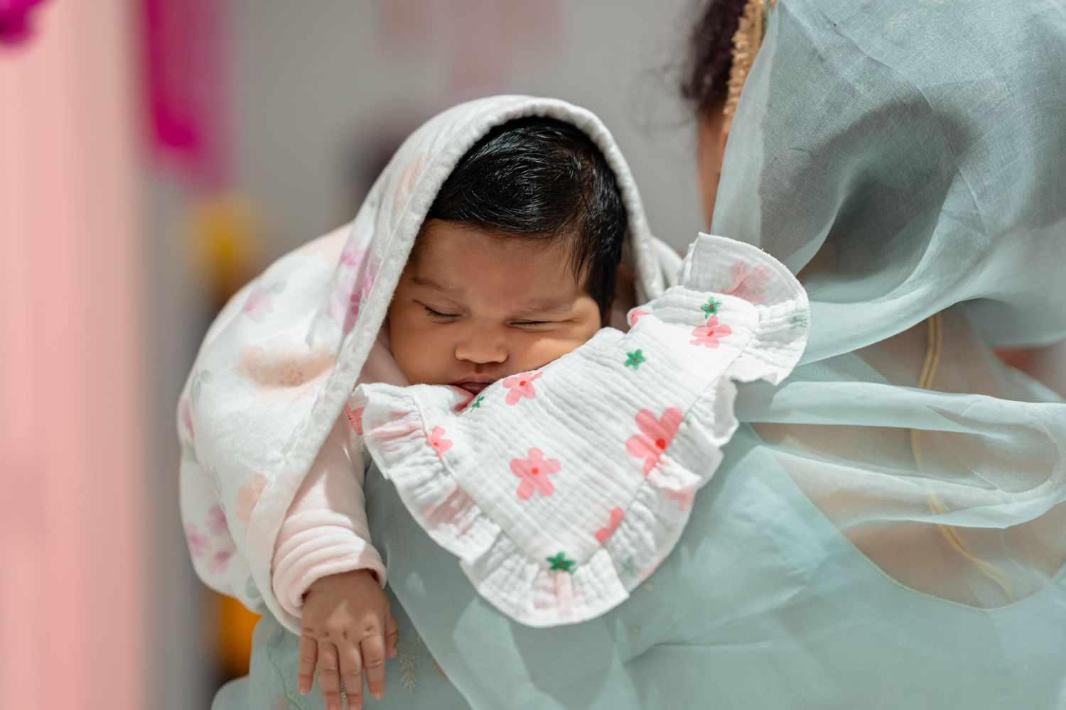 Newborn baby wrapped in a white floral muslin cloth, cradled in arms, peacefully sleeping.