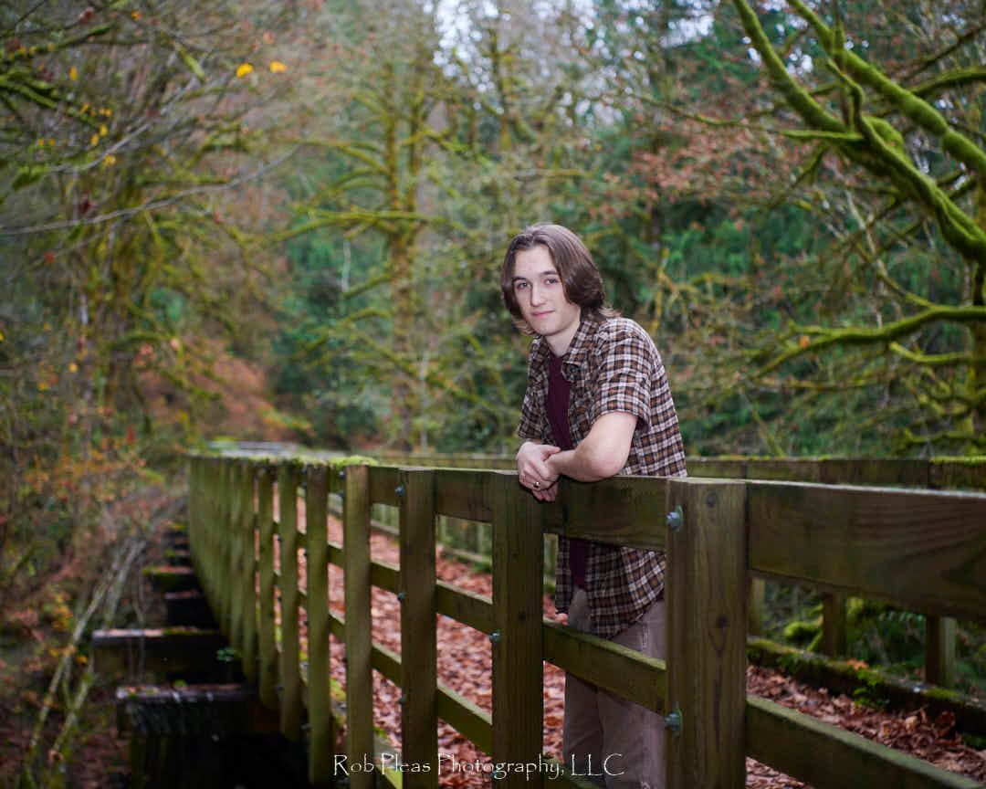 Male high school senior leaning on wooden fence during fall photoshoot.