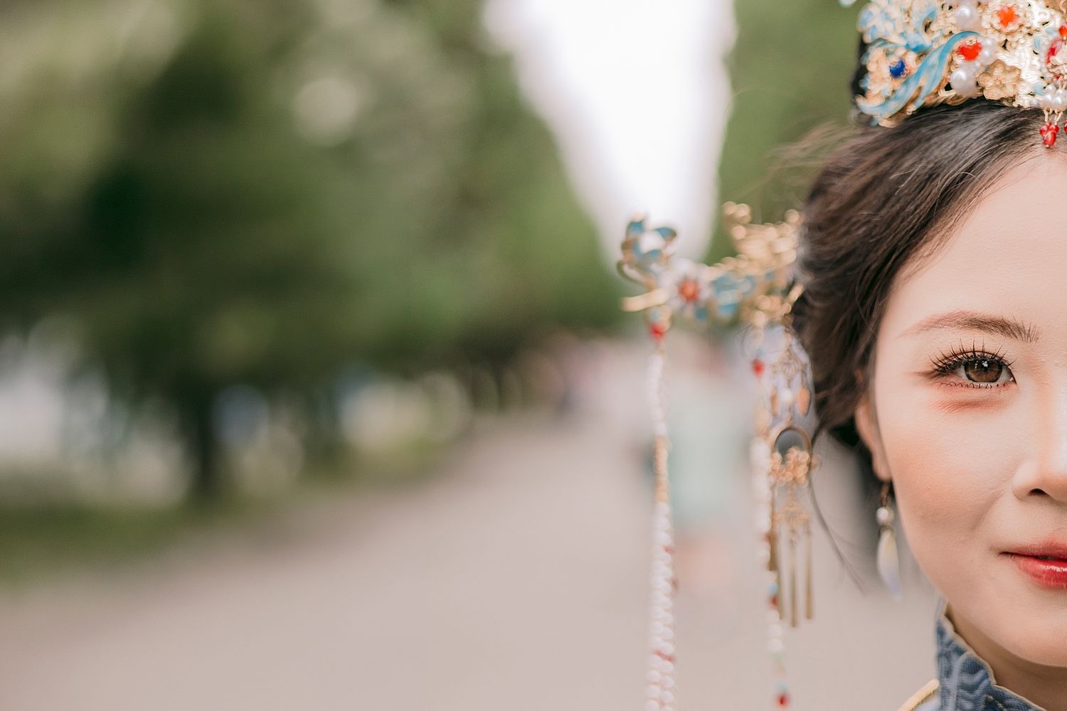Young woman in traditional Chinese attire with ornate floral headdress and elegant makeup, photographed outdoors.