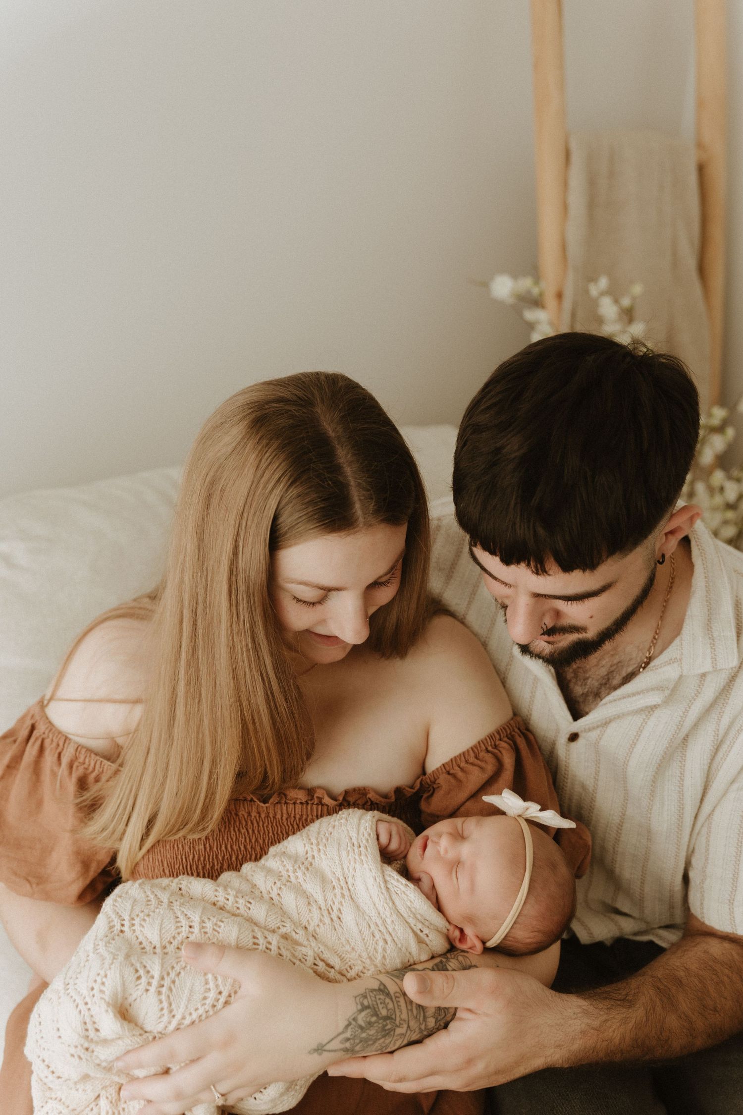 A couple tenderly holds their swaddled newborn baby together in a warm, softly lit room.