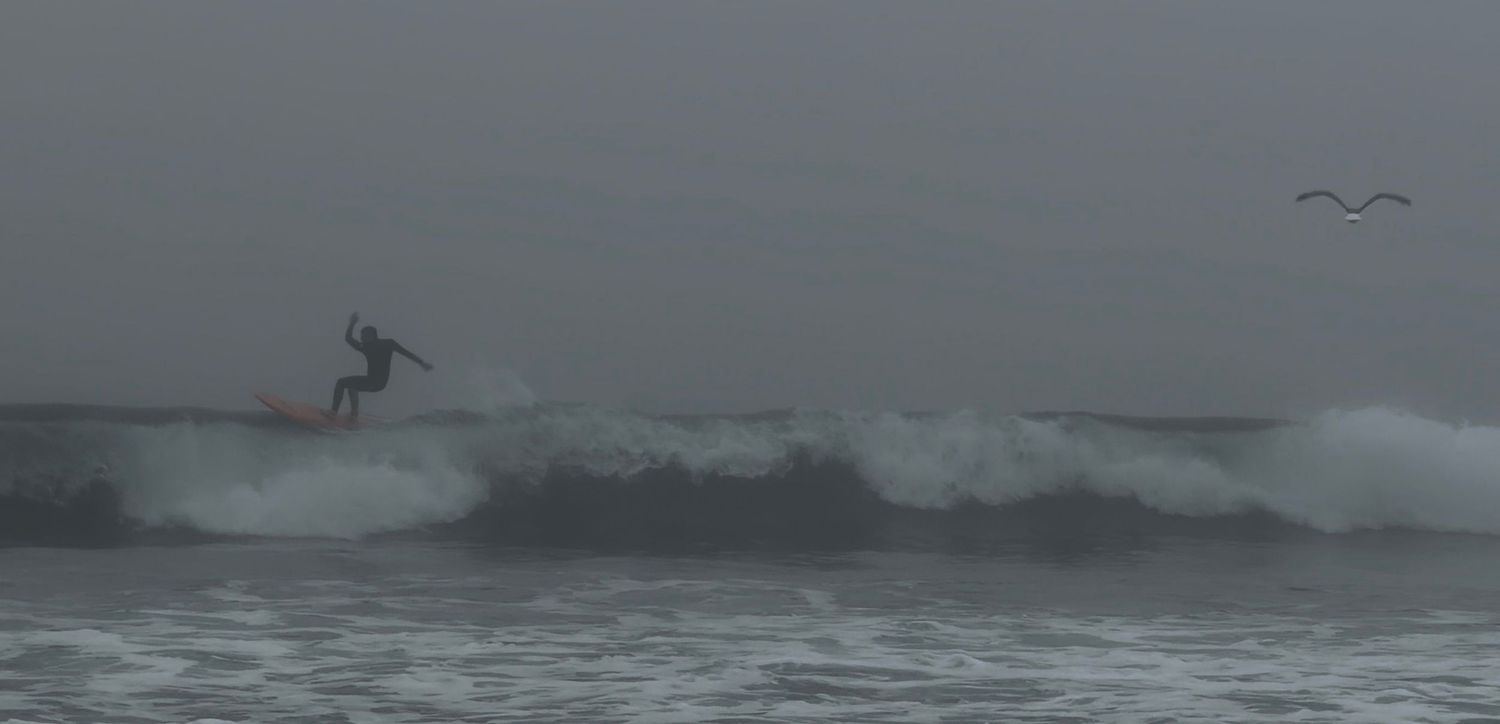 Dramatic aerial view of surfers riding waves in stormy ocean conditions with dark clouds overhead.