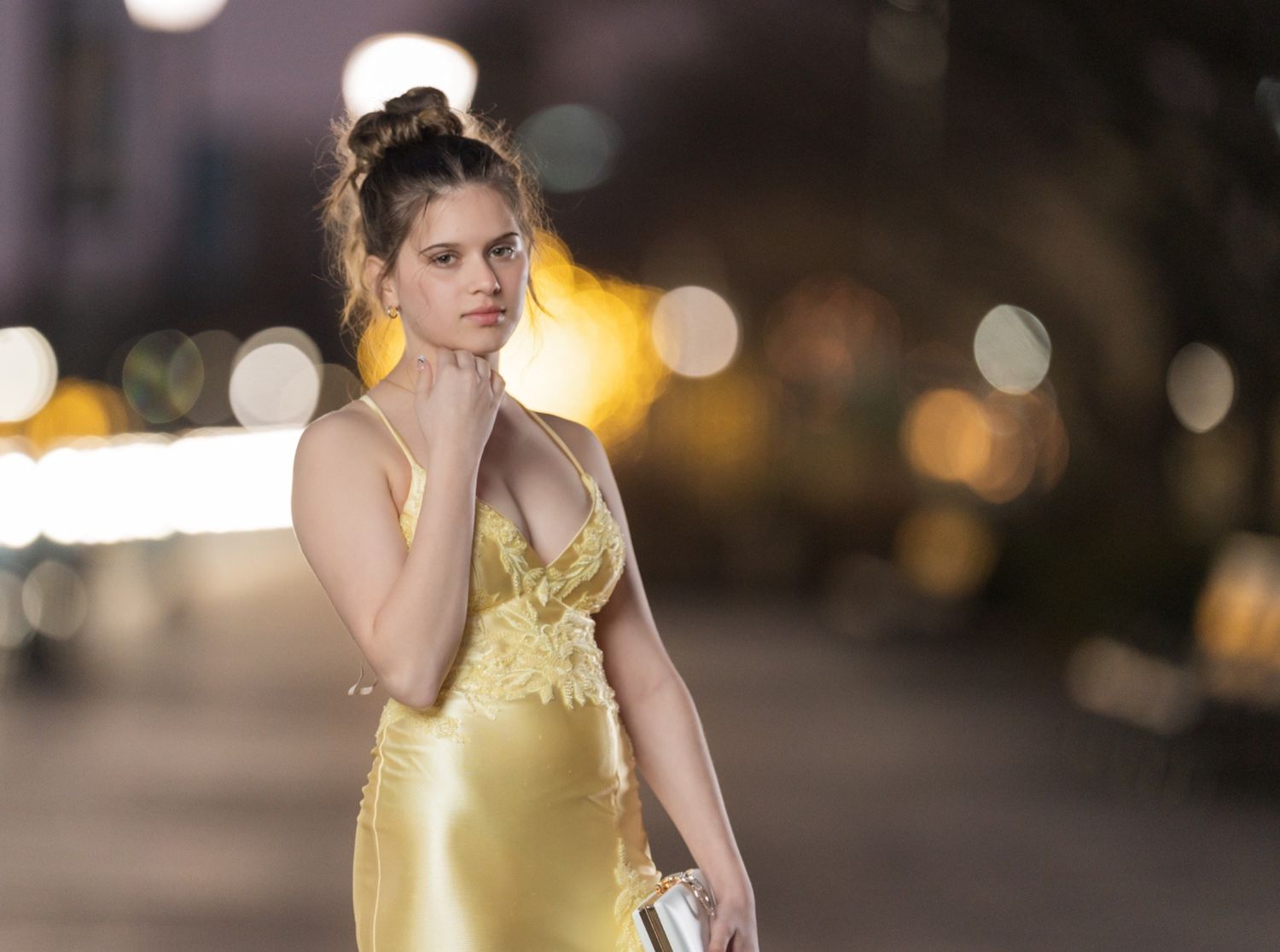 Ava in a yellow prom dress posing at night with glowing bokeh lights at the Wilmington Riverfront in Delaware.