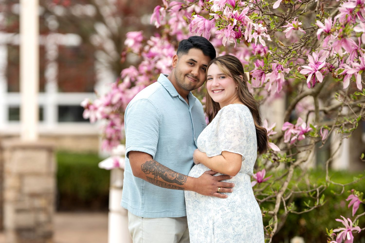 Expecting couple embracing under a blooming pink magnolia tree during a spring maternity photo session.