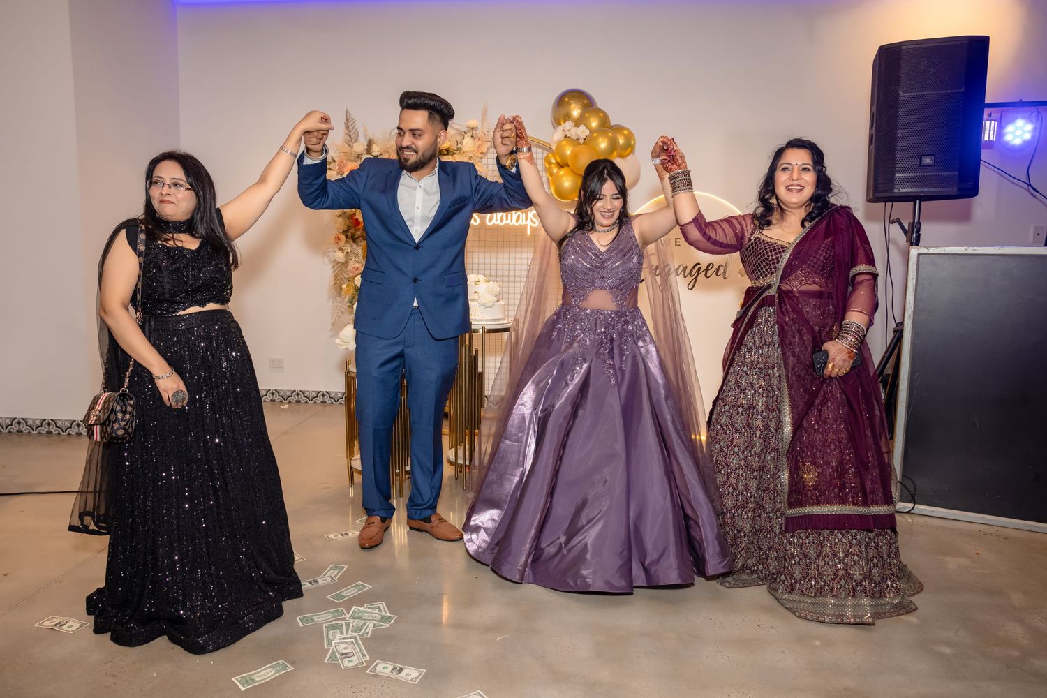 A group of people in formal attire dance together at an elegant event with purple lighting and sparkly decorations.