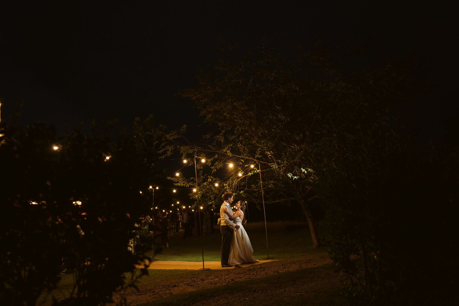 Couple dancing and kissing under fairy lights outdoors at night at a Surrey wedding