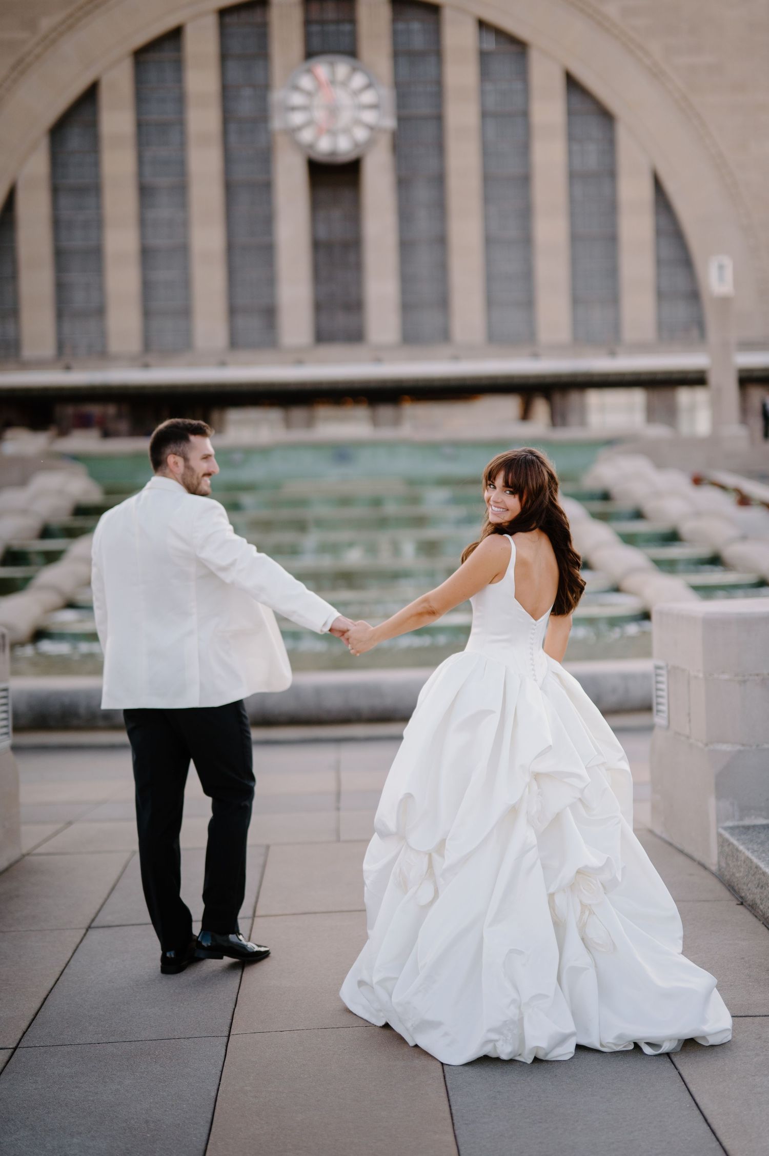 Bride and groom share first dance in elegant venue with colorful mural backdrop, groom in white tuxedo jacket.