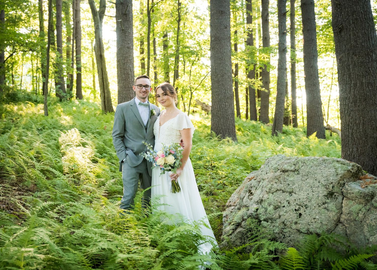 Newlyweds share an intimate moment outdoors with autumn foliage and rustic architecture in background.