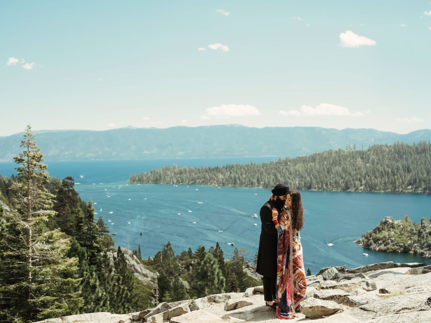 Scenic panoramic view of Lake Tahoe with snow-capped mountains, evergreen forests, and turquoise waters on a sunny day.