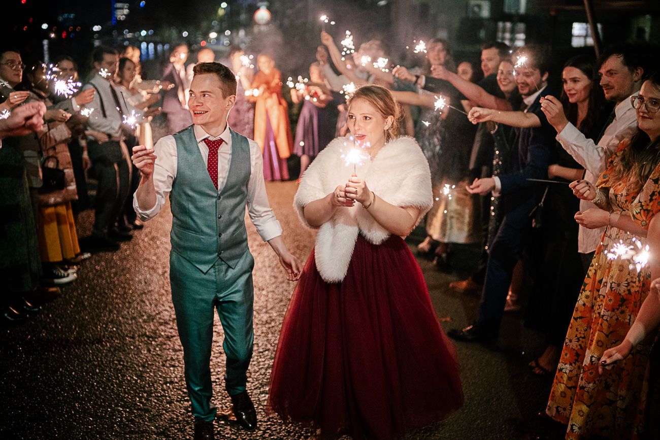 Wedding guests dance and celebrate on a dark dance floor illuminated by sparkling lights during a reception party.