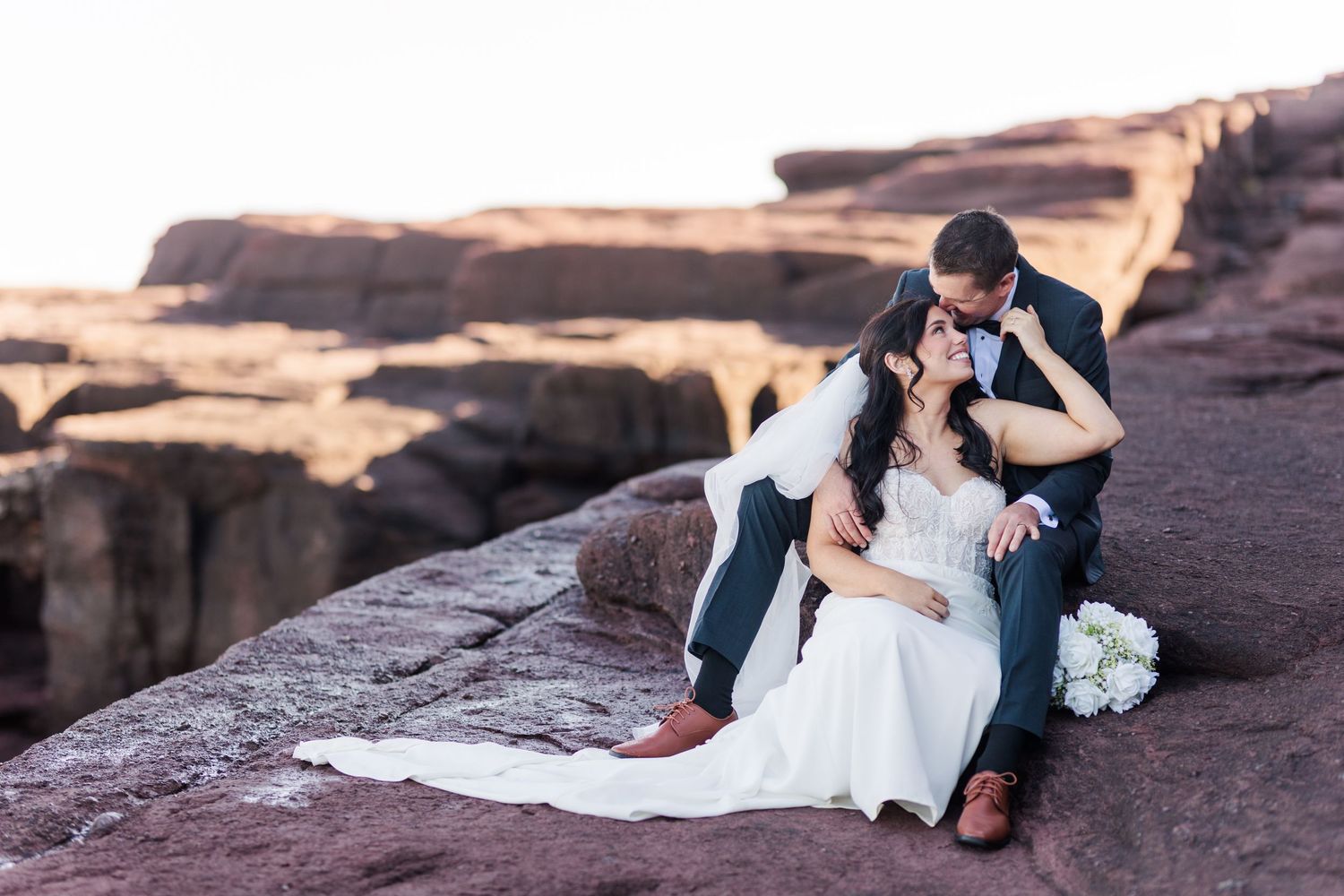 Couple in wedding attire shares intimate moments on red rock cliffs during sunset at Cathedral Rock in Sedona.