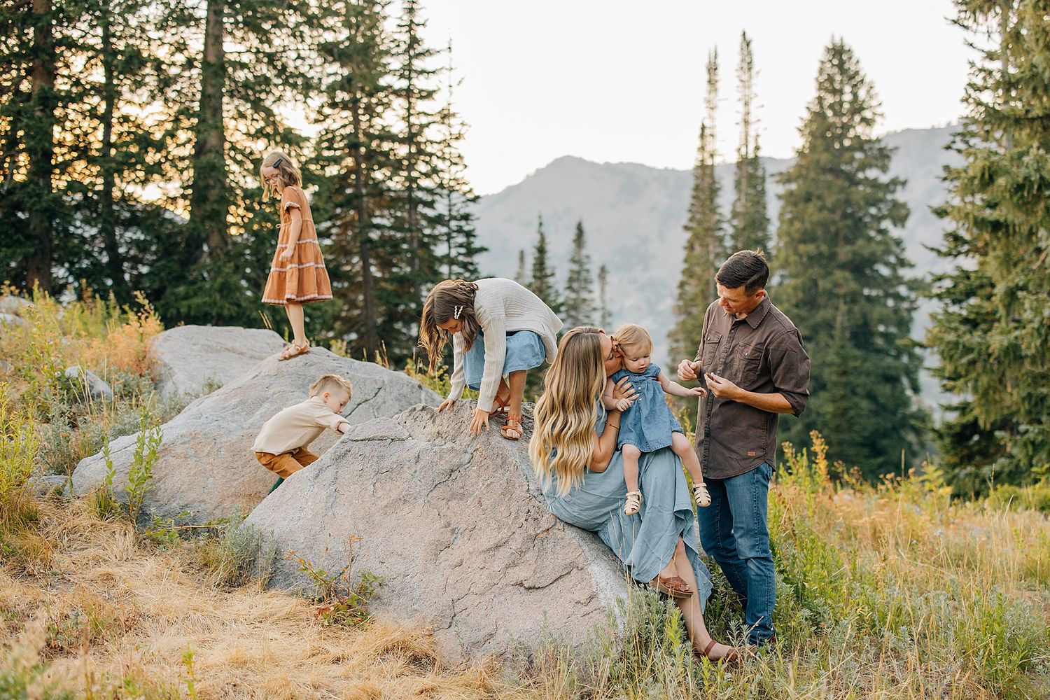 A family in casual attire stands together in a golden-lit field during sunset, sharing joyful moments together.