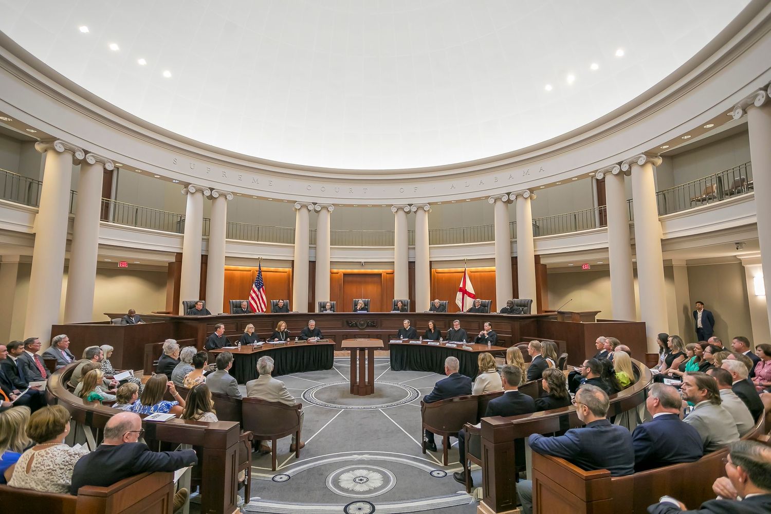 People gathered in a circular legislative chamber with white columns and domed ceiling during a formal session.