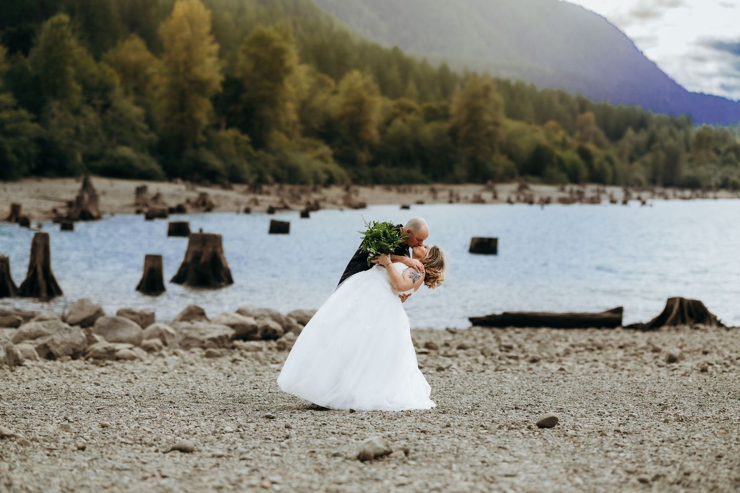 A scenic mountain lakeside view with tree stumps scattered along the rocky shoreline.
