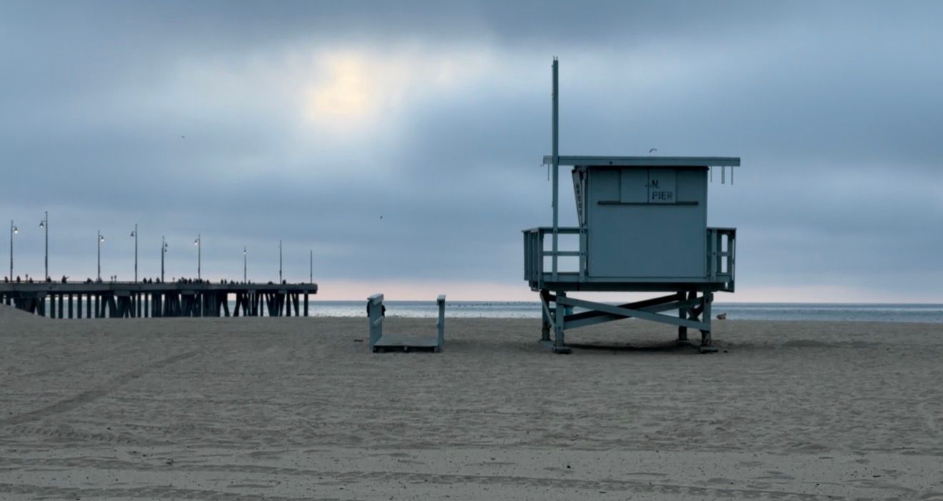 Moody panoramic view of a cloudy beach with a lifeguard tower and wooden pier stretching into the misty ocean.