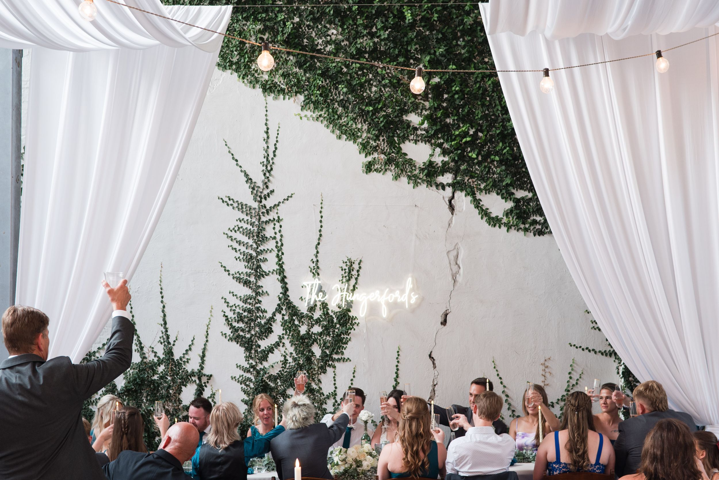 Outdoor wedding ceremony setup with white flowing fabric draped overhead and green trees in the background.