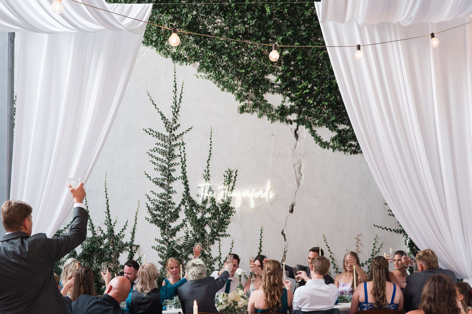 Outdoor wedding ceremony setup with white flowing fabric draped overhead and green trees in the background.