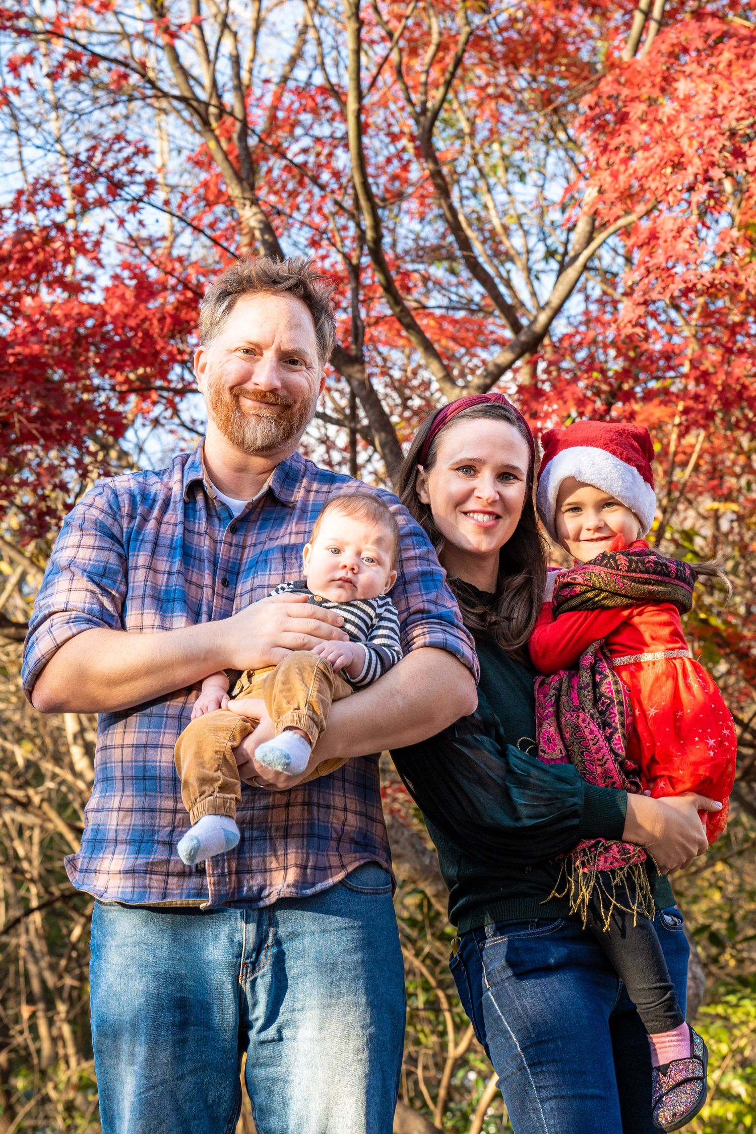 Family enjoys time together in autumn foliage with colorful red maple trees in the background.