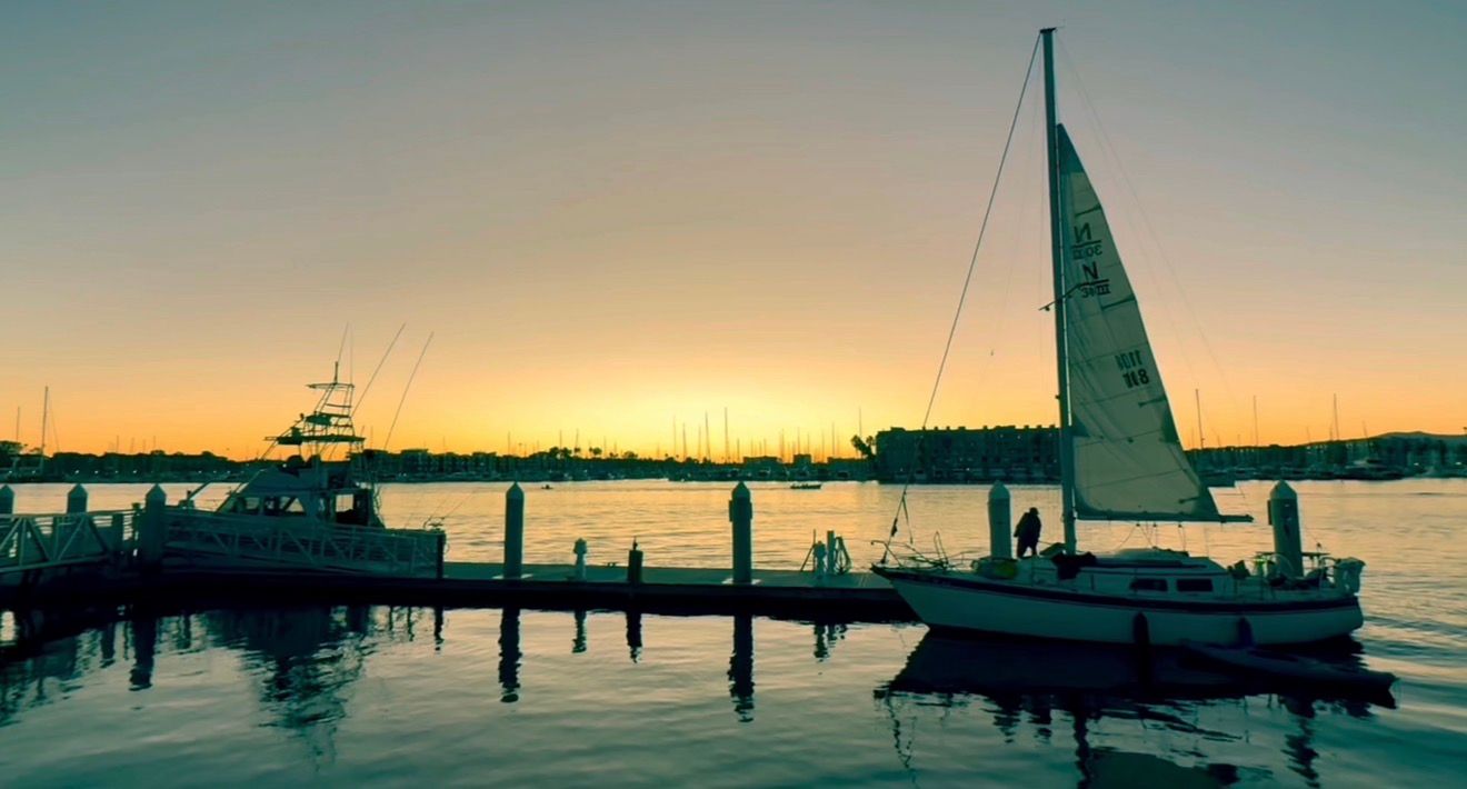 Sailboats and yachts docked at a marina during a tranquil sunset with golden light reflecting on calm waters.