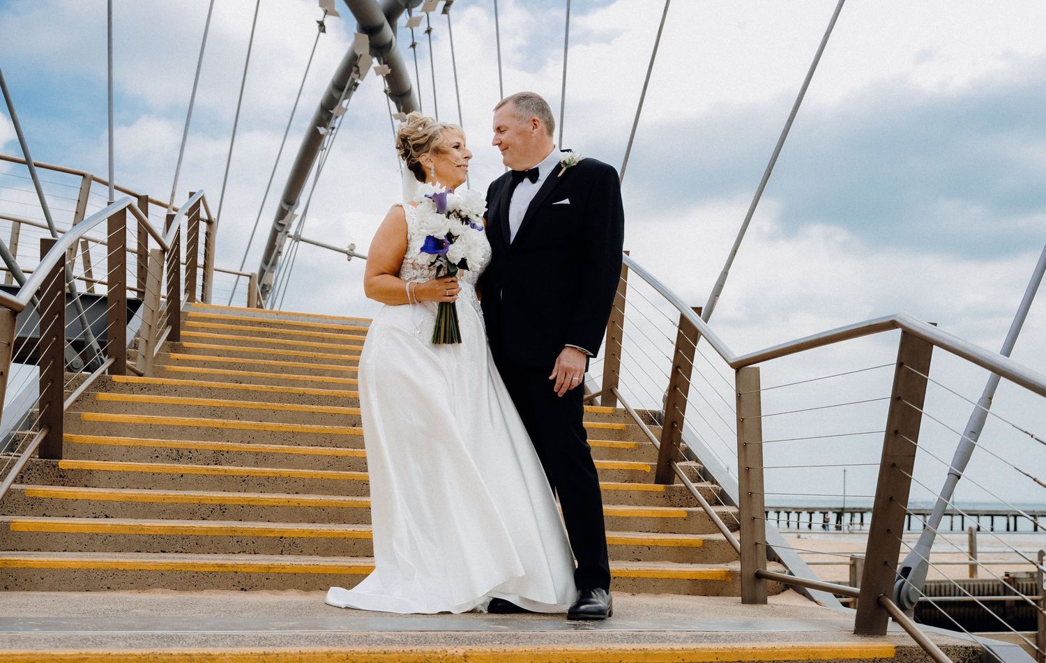A composite of five wedding photos showing a couple on a rustic wooden pier descending stairs by the ocean.