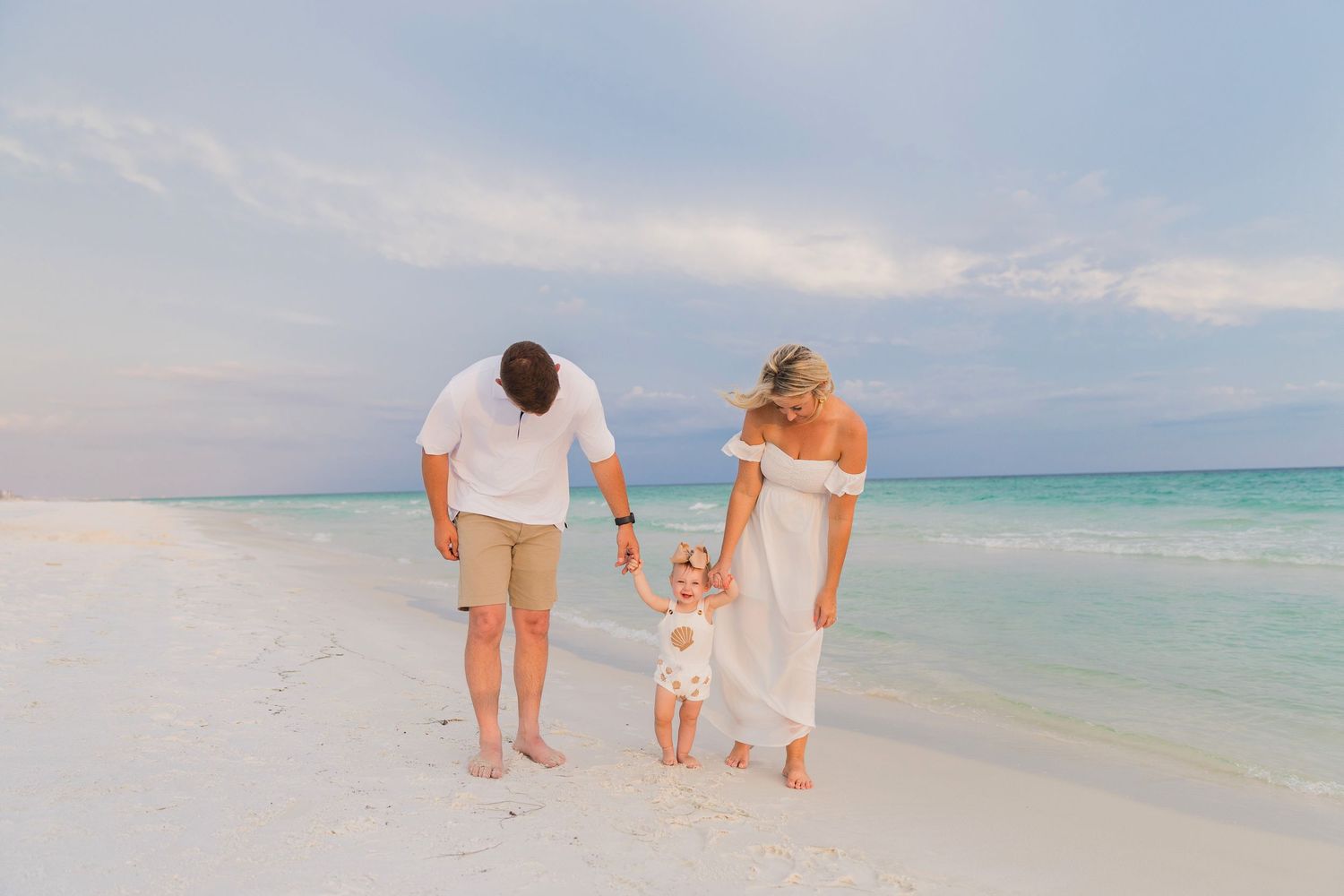 A family wearing white outfits shares a playful moment together on a sandy beach.