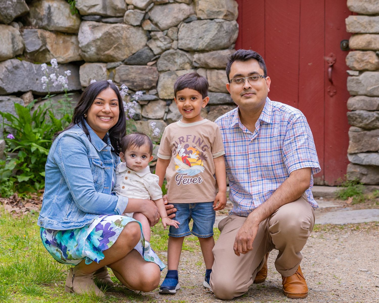 A collection of family portraits taken against a rustic red door and stone wall backdrop on a sunny day.