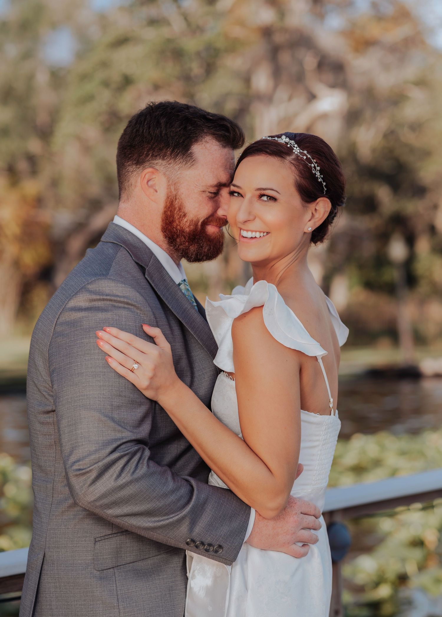 A smiling couple embraces during their outdoor wedding photoshoot in a scenic garden setting.