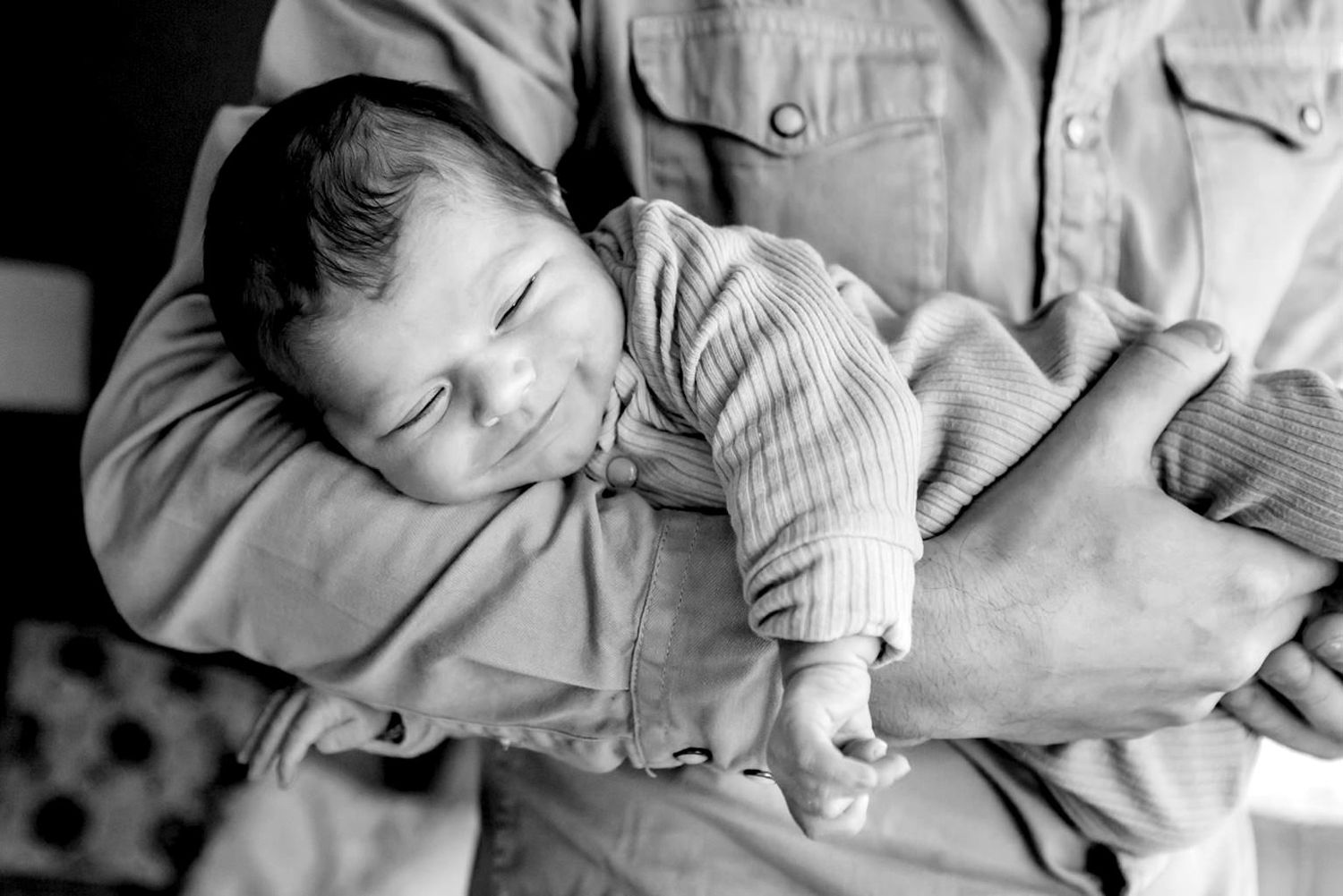 Baby liggend op de buik op de arm van papa tijdens een lifestyle newbornshoot, vastgelegd in een rustig en liefdevol moment