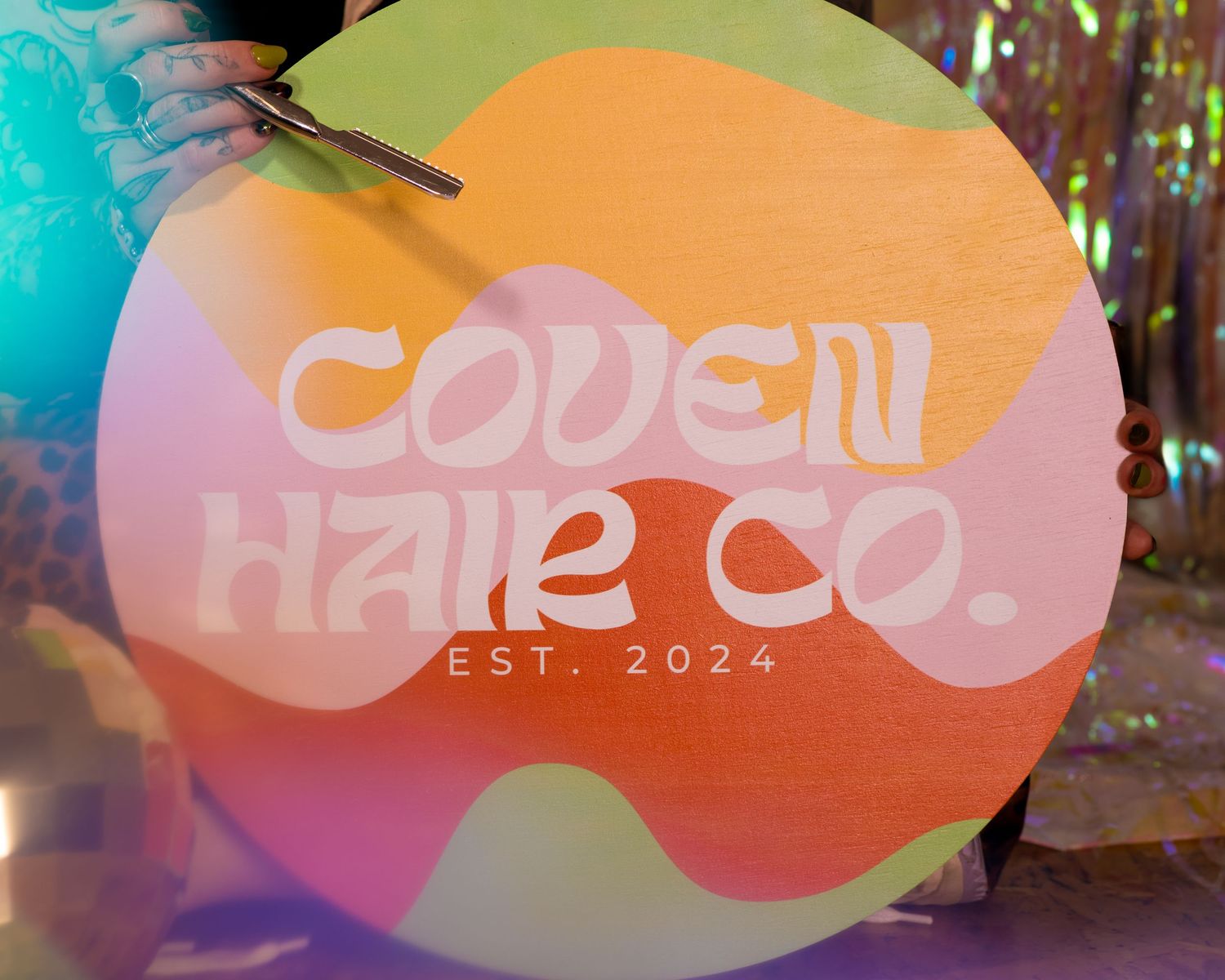 Colorful round wooden sign reading Coven Hair Co. Est. 2024 with pastel wave design.