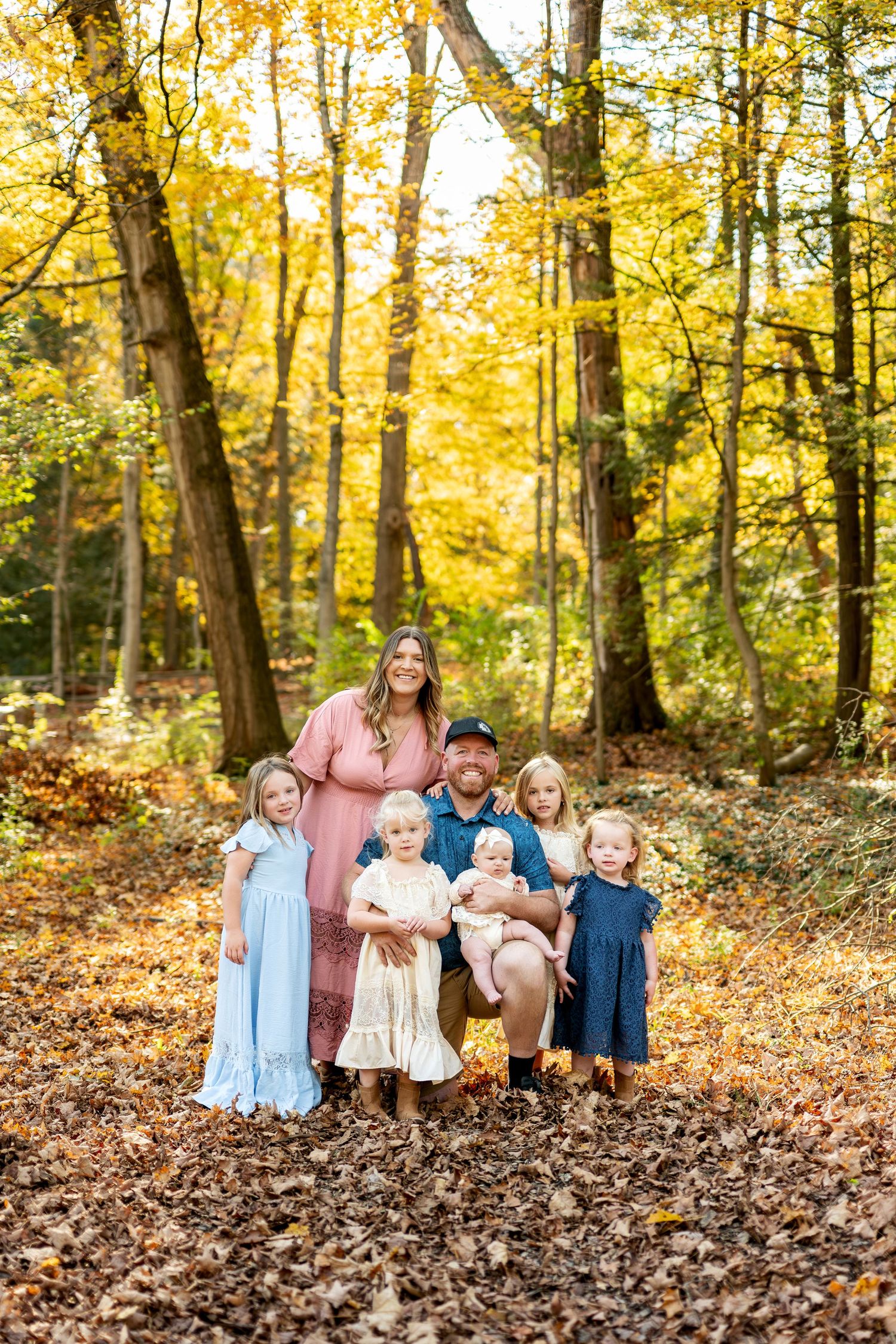 A family of seven with four young daughters and a baby poses in a stunning golden autumn forest.
