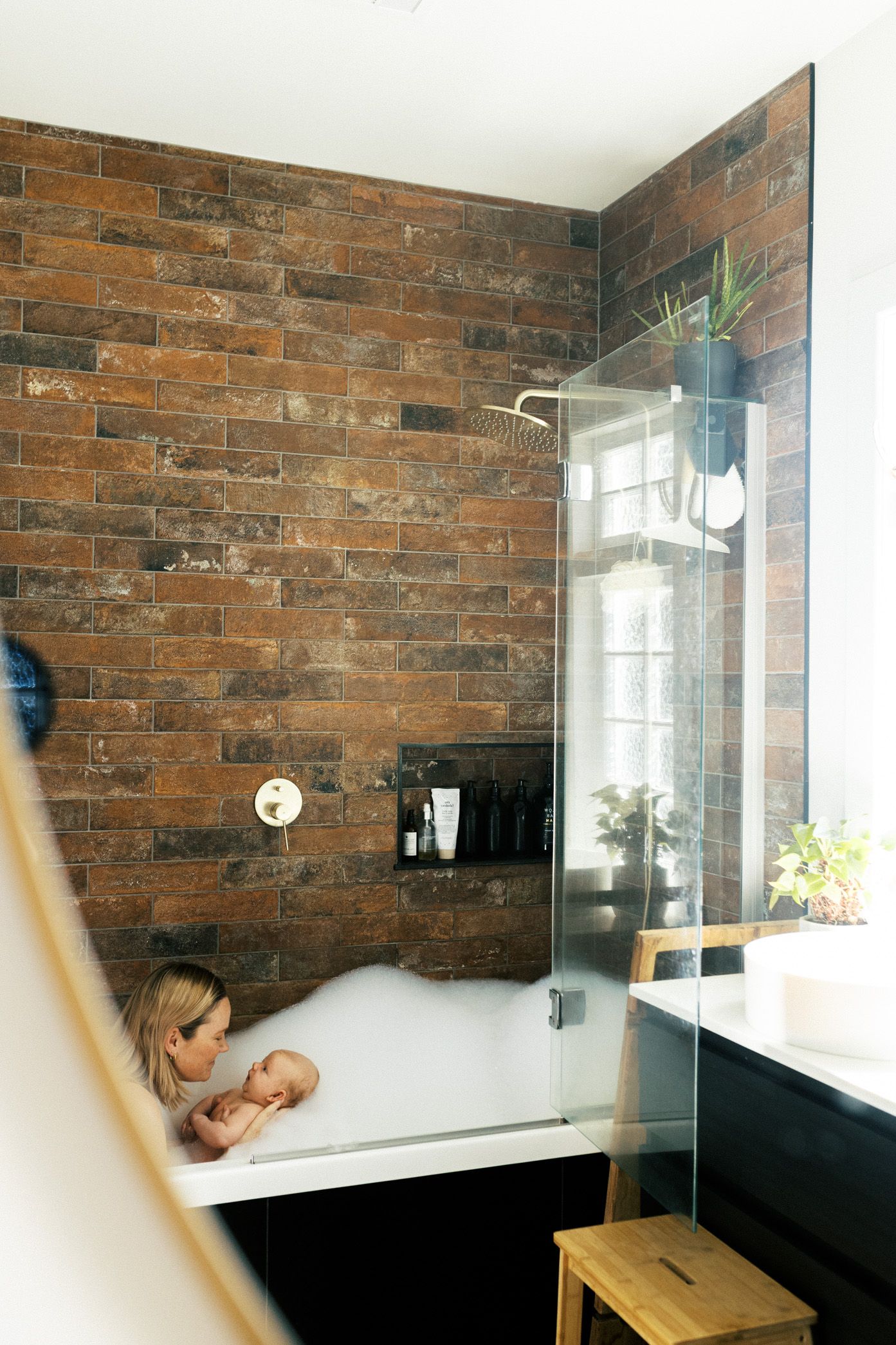Modern bathroom interior with exposed brick walls and glass shower enclosure features natural light from window.
